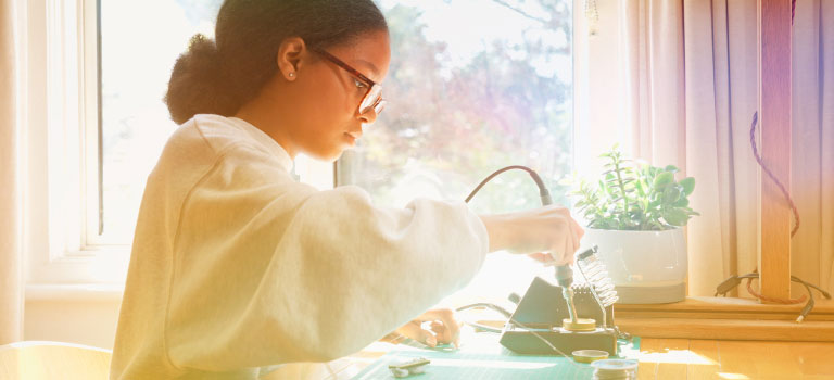 Young African American girl concentrating on a STEM project at her home desk by a sunny window